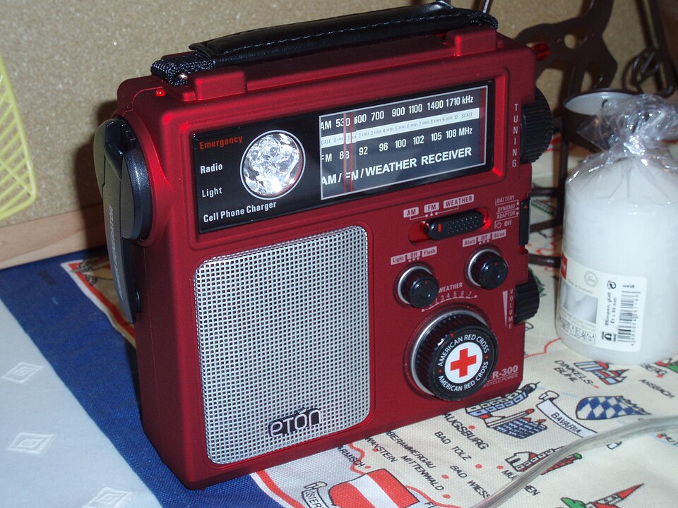 A red Eton emergency radio with a tuning dial, speaker grille and hand crank, for storm prep in Daphne, AL